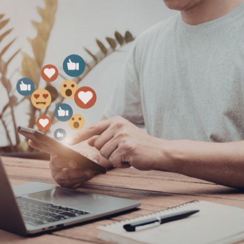 Fotografija prikazuje računalnik in telefon z ikonami srčkov in všečkov, simbol uspeha na družbenih omrežjih