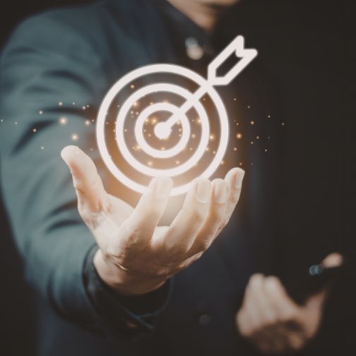 Fotografija prikazuje odprto dlan in cilj s krogi ter puščico, ki zadene sredino cilja, simbol uspeha in doseganja ciljev